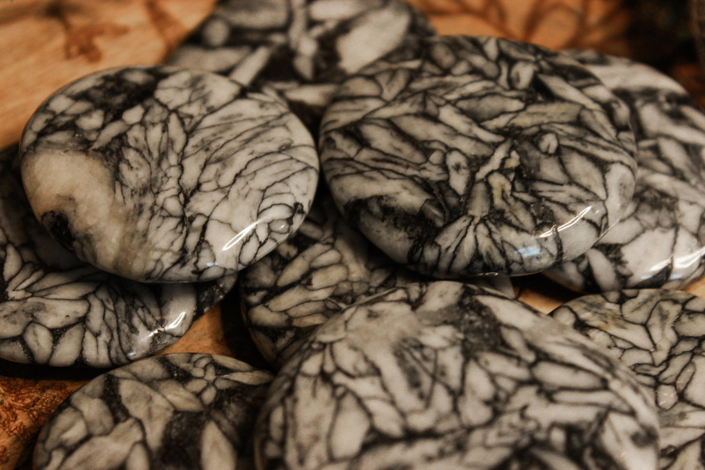 Eisblumen-Magnesit Scheibenstein aus Österreich - Faire regionale Steine - Mehrere schwarze weiße und glatte Eisblumen-Magnesit Pinolith auf einem Holztisch