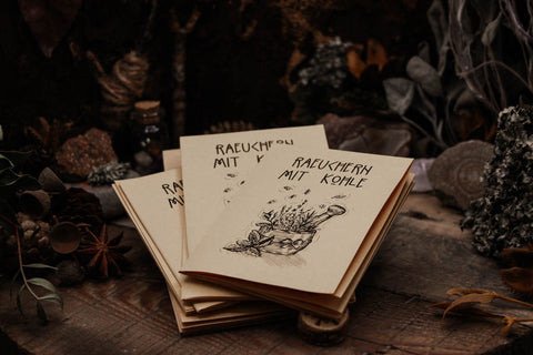Mehrere kleine Zine, Anleitung mit Bildern zum Räuchern, das Papier sieht gelblich aus mit schwarzer Schrift. auf einem dunklen Tisch umgeben von Kräutern und Kristallen