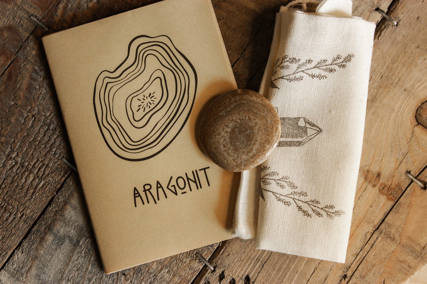 Aragonit Scheibenstein aus Österreich - Faire regionale Steine -ARAGONIT mit kleiner bedruckter Tasche und einem kleinen ARAGONIT Booklet auf einem Holztisch