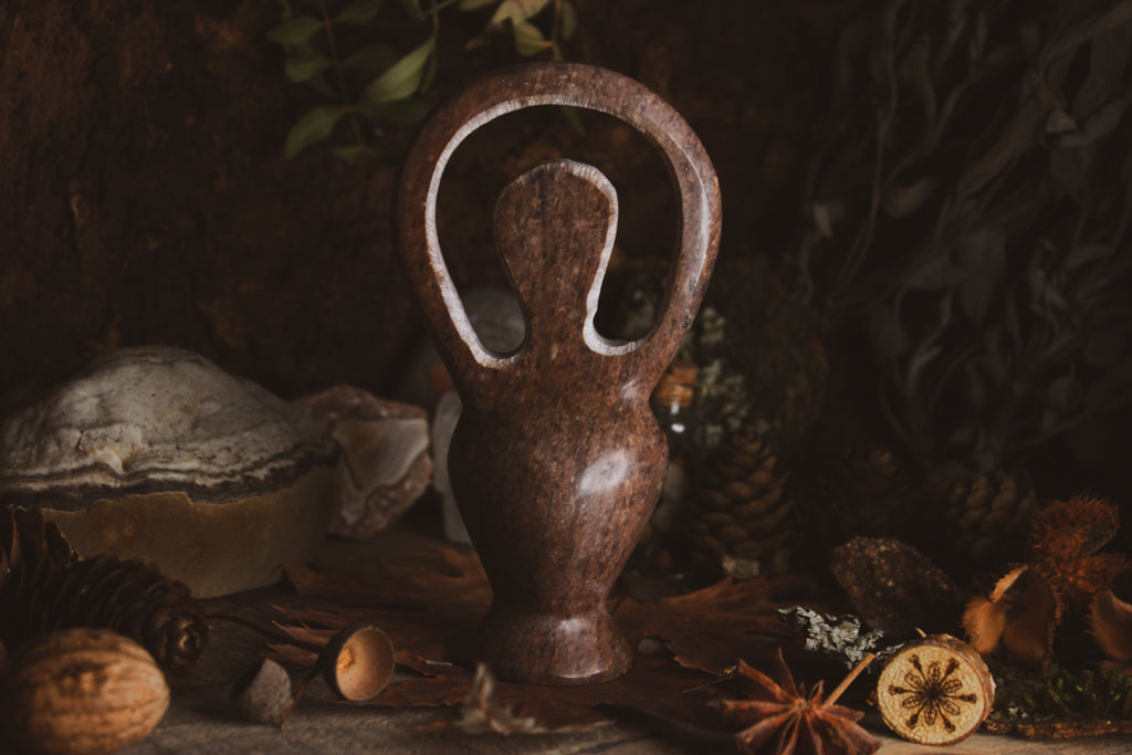 Eine kunstvoll gestaltete Skulptur, Göttinenfigur, dunkelbraun und poliert präsentiert in einer natürlichen Umgebung mit getrockneten Blättern und Sternanis.