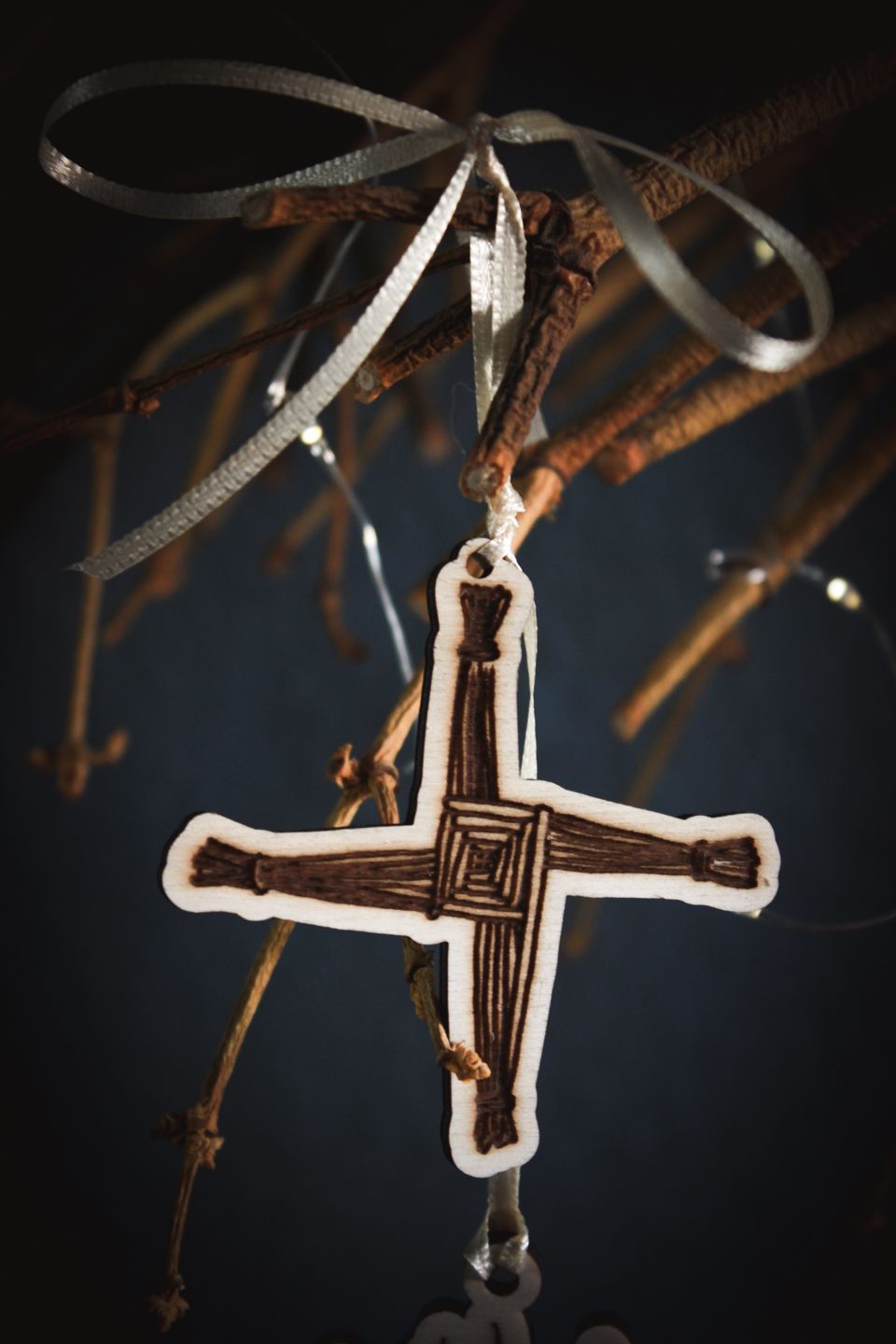 Eine Nahaufnahme des Kreuzes der Brigid an einer hellgelben Schnur. Das Brigids Corss ist aus Holz und das Motiv eingebrannt.