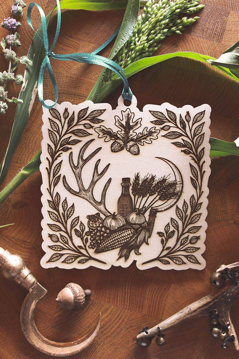 Hochkant: Herbstliches Holzornament zum Aufhängen mit filigraner Gravur zu Mabon. Zeigt Erntemotive wie Getreide, Mais, Eicheln und Trauben, sowie einen kleinen Hamster, eingerahmt von Hirschgeweihen, Hagebuttenzweigen und einer Erntesichel. Mit türkisfarbenem Band und rustikalem Flair. Ideal für saisonale Dekoration und spirituelle Rituale zur Herbsttagundnachtgleiche.