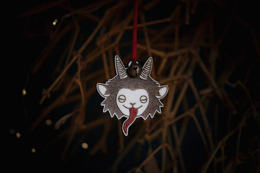 Vor einem Mistelstrauch hängt an einem roten Faden mit Glöckchen ein Holz-Ornament, das den niedlichen Kopf eines Krampus mit langer roter Zunge und Hörnern eingebrannt hat.