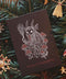 Hochkant: Gebettet auf Tannenzweigen und weihnachtlicher Dekoration liegt in der Mitte eine schwarze Karte mit weiß-rotem Aufdruck. Das Motiv zeigt einen Krampus, der zwischen Fliegenpilzen sitzt. Er hat einen Pentagramm-Ohrring am Ohr, eine große Glocke um den Hals und hält eine Rute aus Zweigen in der Klaue. In roter Schrift steht darunter: Gruß vom Krampus