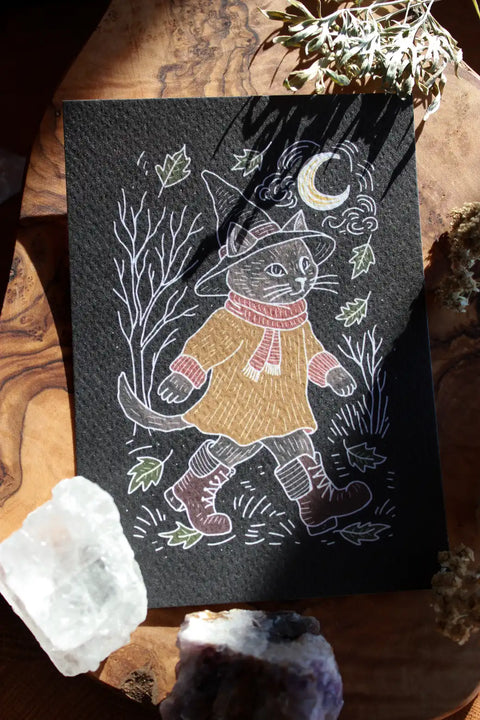 Der Print zeigt eine Katze mit Hexenhut, die im Mondschein durch eine Herbstlandschaft spaziert.