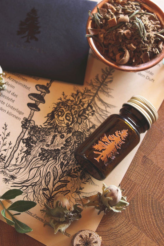 Rustikale Anordnung aus einer Braunglasflasche mit Baumemblem und Räucherwerk, einer Schale getrockneter Kräuter, einer detaillierten schwarz‑weißen Waldwesen‑Illustration (ein Moosweiblein) sowie Nüssen und Blättern auf Papier mit Schrift.