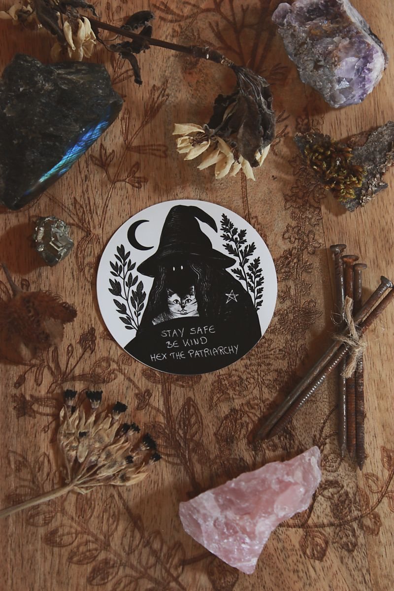 Ein runder Sticker mit Message, die lautet: Stay Safe Be Kind Hex The Patriarchy
Die vermummte Hexen-Gestalt mit Hexen-Hut, hält eine Katze in den Armen. Auf ihrer Schulter ist ein kleines Pentagramm zu sehen. Um sie herum sind Salbei und Beifuß.