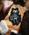 Ein schwarz-weißer Sticker der eine Katze im Skelett-Kostüm zeigt. Die Katze trägt einen Kürbis-Eimer in der Hand.