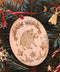 Hochkant: Gebettet auf Tannenzweigen und weihnachtliche Dekoration liegt in der Mitte ein ovales Ornament aus Holz. Diese Dekoration zu Jul (Wintersonnenwende) zeigt ein Wildschwein. Eingerahmt wird es von typischen Jul-Motiven wie Mistelzweigen, Stechpalmen, Strohsternen, Geweihen und passenden Runen.