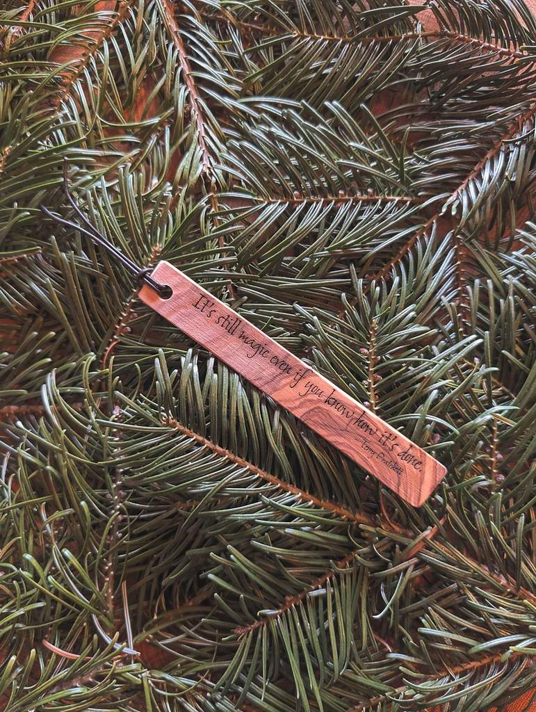 Ein Lesezeichen aus Holz auf dem ein Zitat eingraviert ist: It's still magic even if you know how it's done. Terry Pratchett