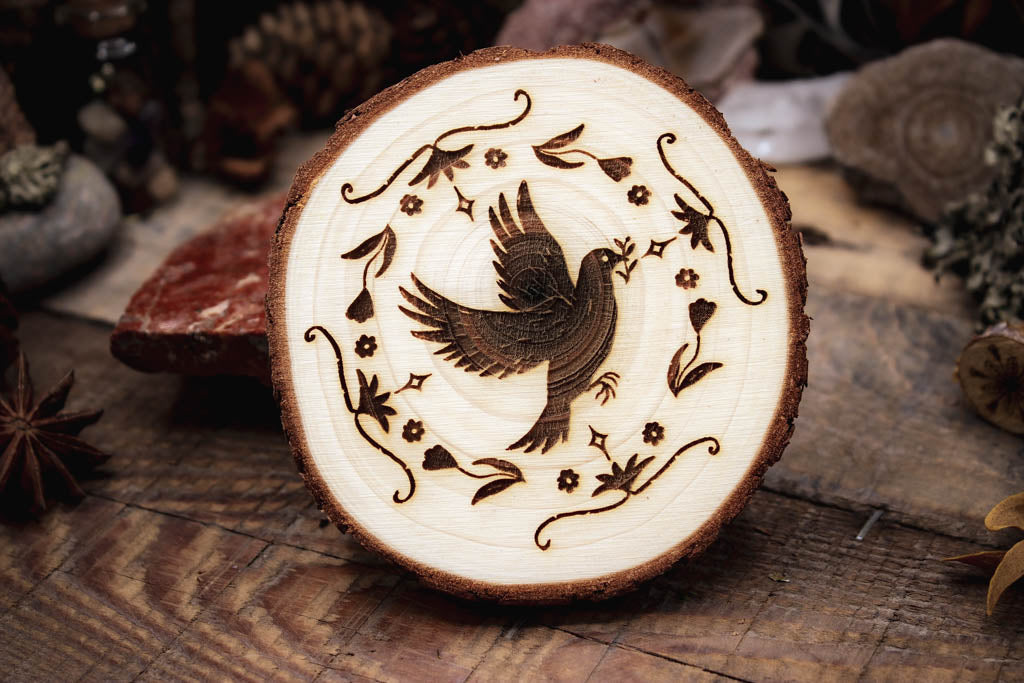 Holzgravur-Taube-Taubenhilfe, eine Taube umgeben vor mehreren Designelementen fliegt und trägt eine Pflanze im Schnabel, präsentiert in einer rustikalen Umgebung mit Kiefernzapfen,