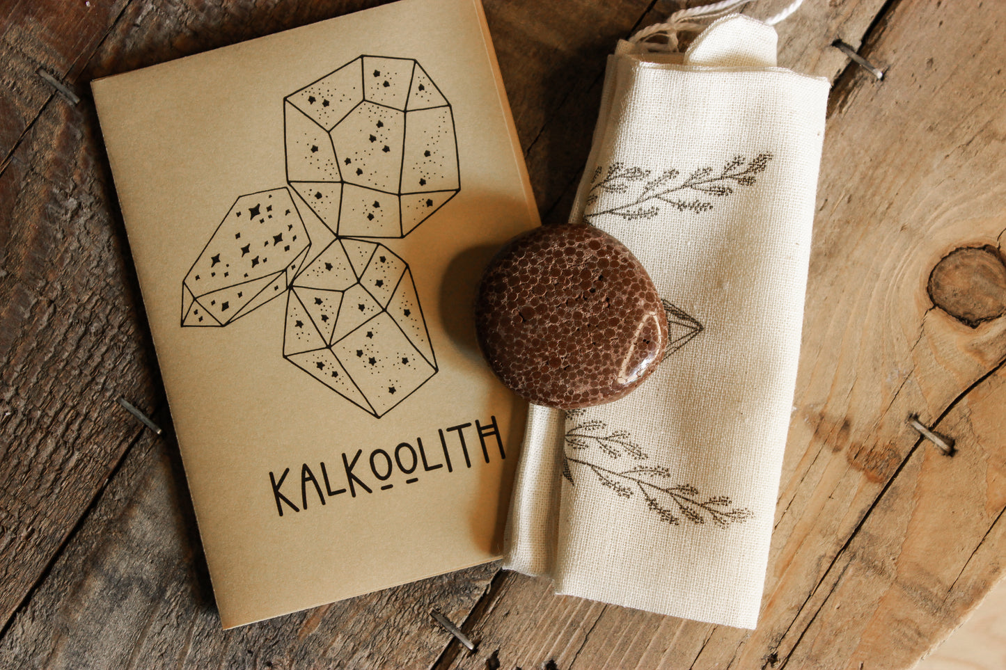 Kalkoolith Scheibenstein aus Deutschland - Faire regionale Steine - Kalkoolith -Kalkoolith mit kleiner bedruckter Tasche und einem kleinen Kalkoolith Booklet auf einem Holztisch