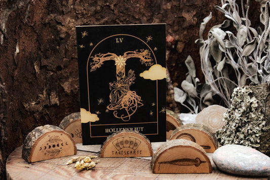 Verschiedene Kartenaufsteller mit witchy Motiven aus Holz mit rustikaler Rinde. In der Mitte ist auf einem ein Motiv eingebrannt, dass Karten und das Wort Tageskarte zeigt. Im Aufsteller steckt eine schwarze Tarotkarte, die eine Frau die unter einem Baum spinnt zeigt.