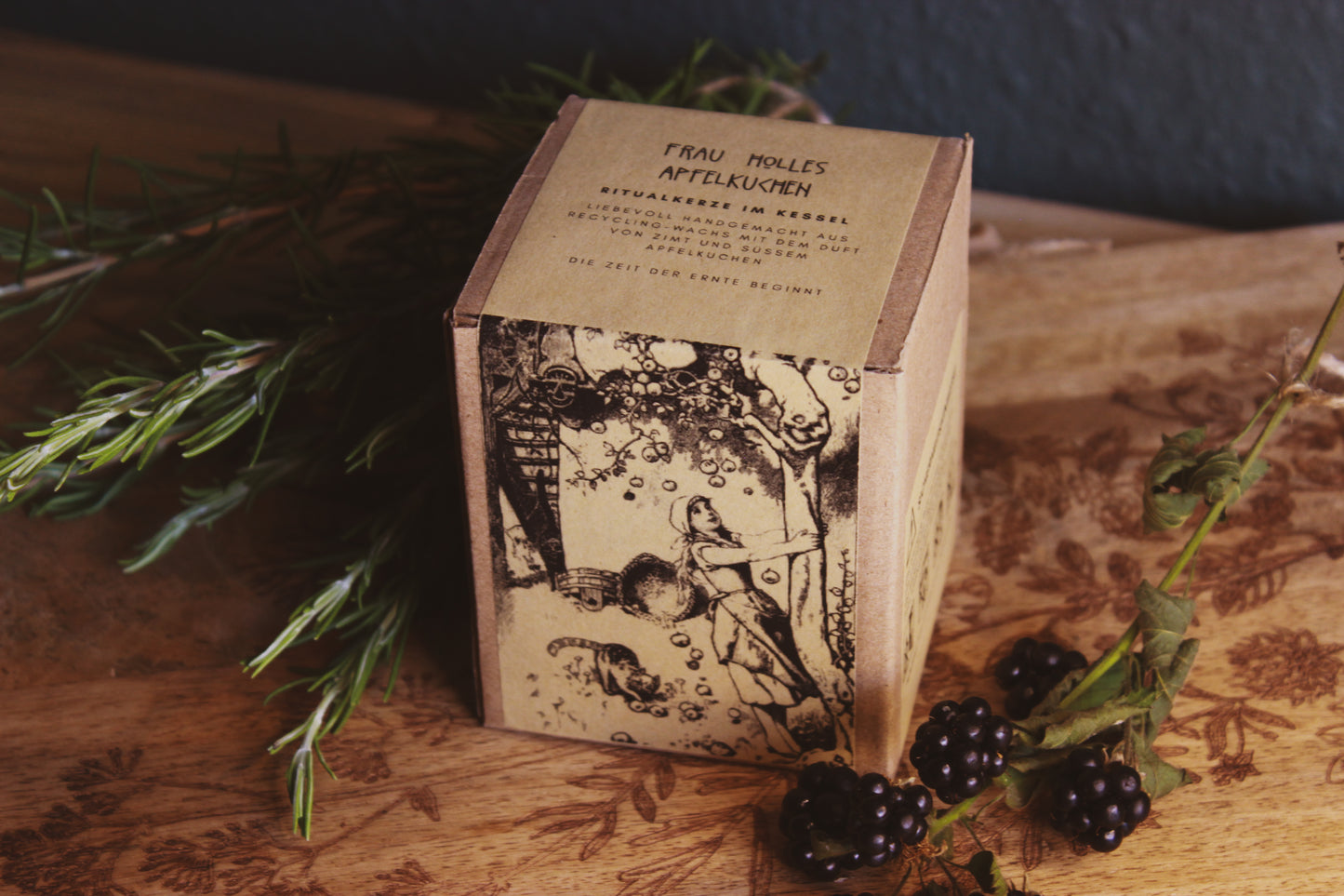 Nachhaltige Verpackung von "Frau Holles Apfelkuchen" darunter eine Abbildung von einer Frau die einen Baum schüttelt, umgeben von Kräutern und Beeren, alles wurde schön auf einem braunen Brettchen präsentiert