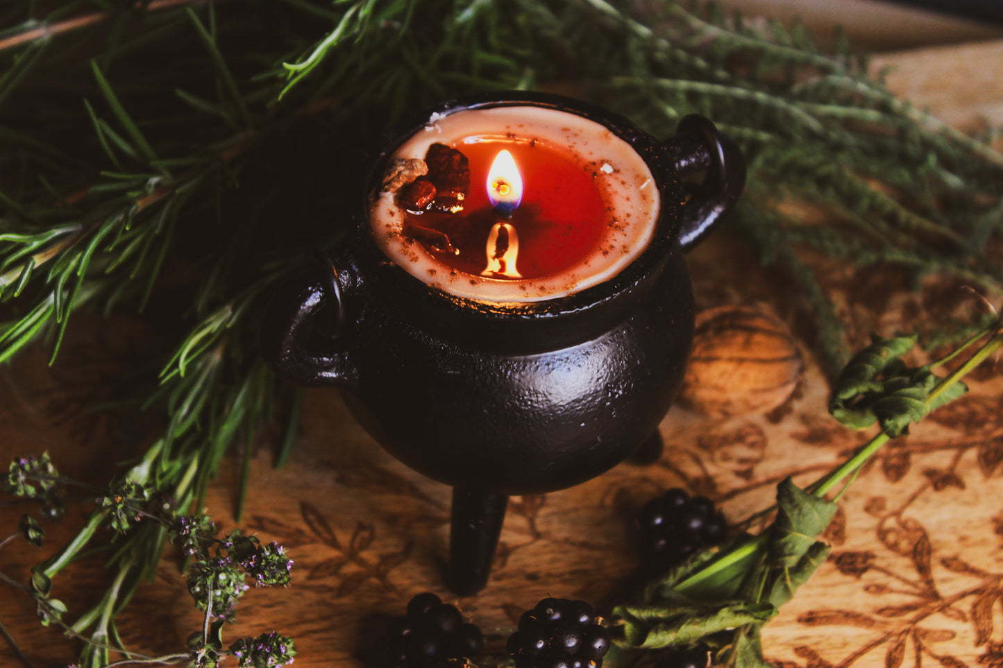 Nahaufnahme, Schwarzer Kessel mit rotem Wachs, die Kerze wurde entzündet umgeben von Kräutern und Beeren, alles wurde schön auf einem braunen Brettchen präsentiert