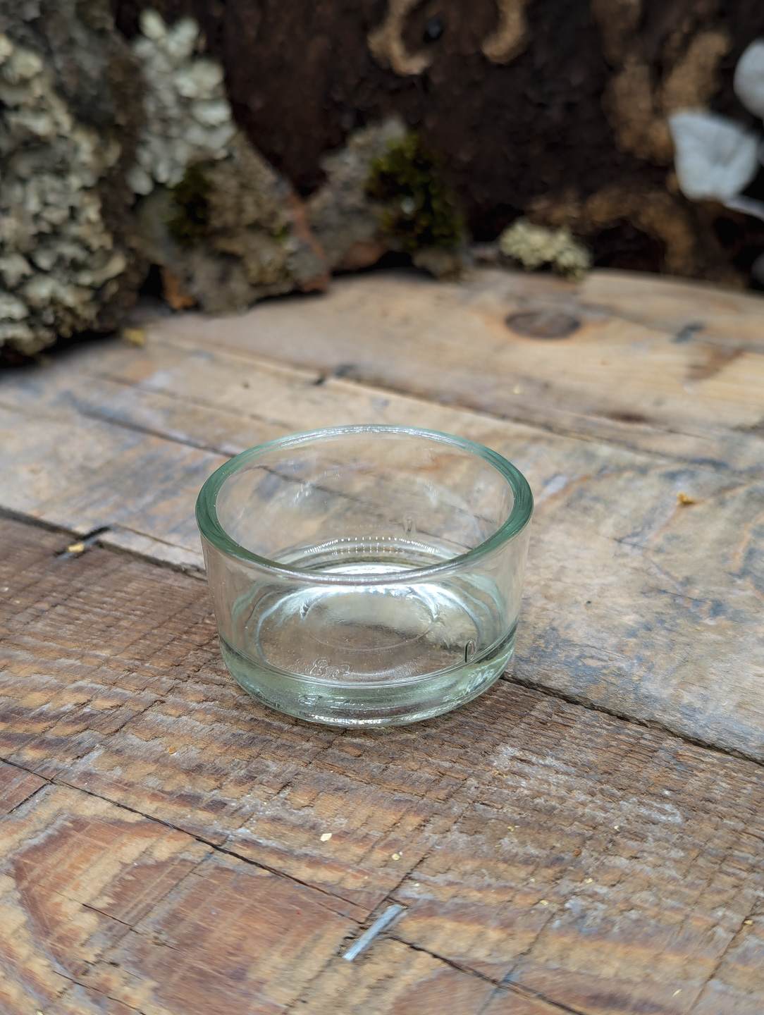 Auf einem Holzbrett steht ein schlichter Teelichthalter aus dickem Glas.