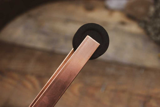 Eine Räucherzange aus Kupfer hält ein Stück Kohle.