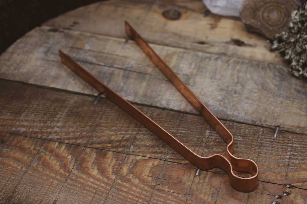 Eine Räucherzange aus Kupfer liegt auf einem Holzbrett.