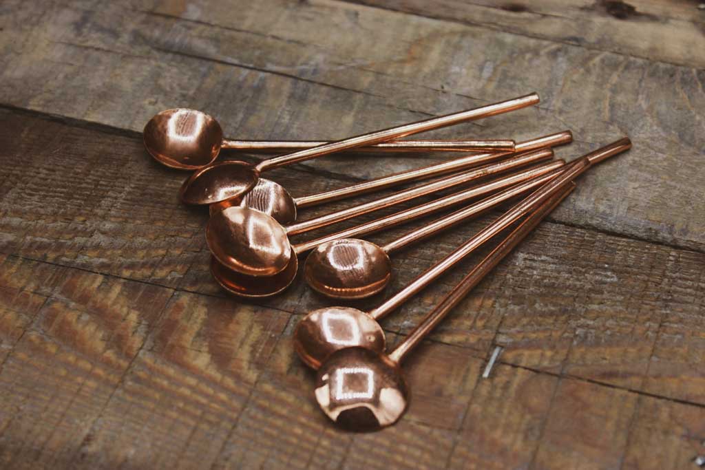 Mehrere Kupferlöffel liegen auf einem Holzbrett.