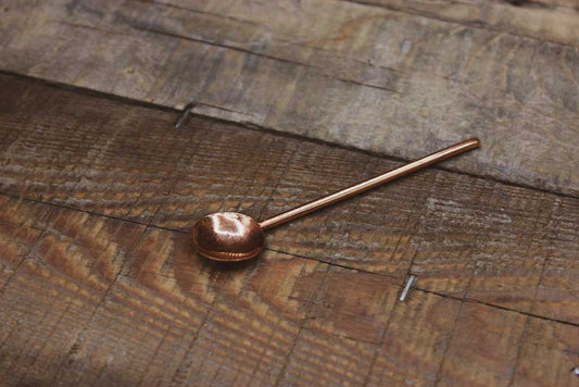 Ein Kupferlöffel liegt auf einem Holzbrett.