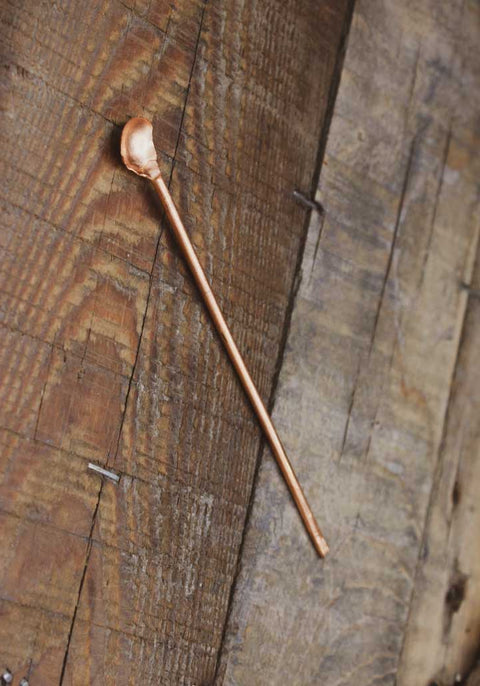 Ein schmaler langer Kupferlöffel auf einem Holzbrett.