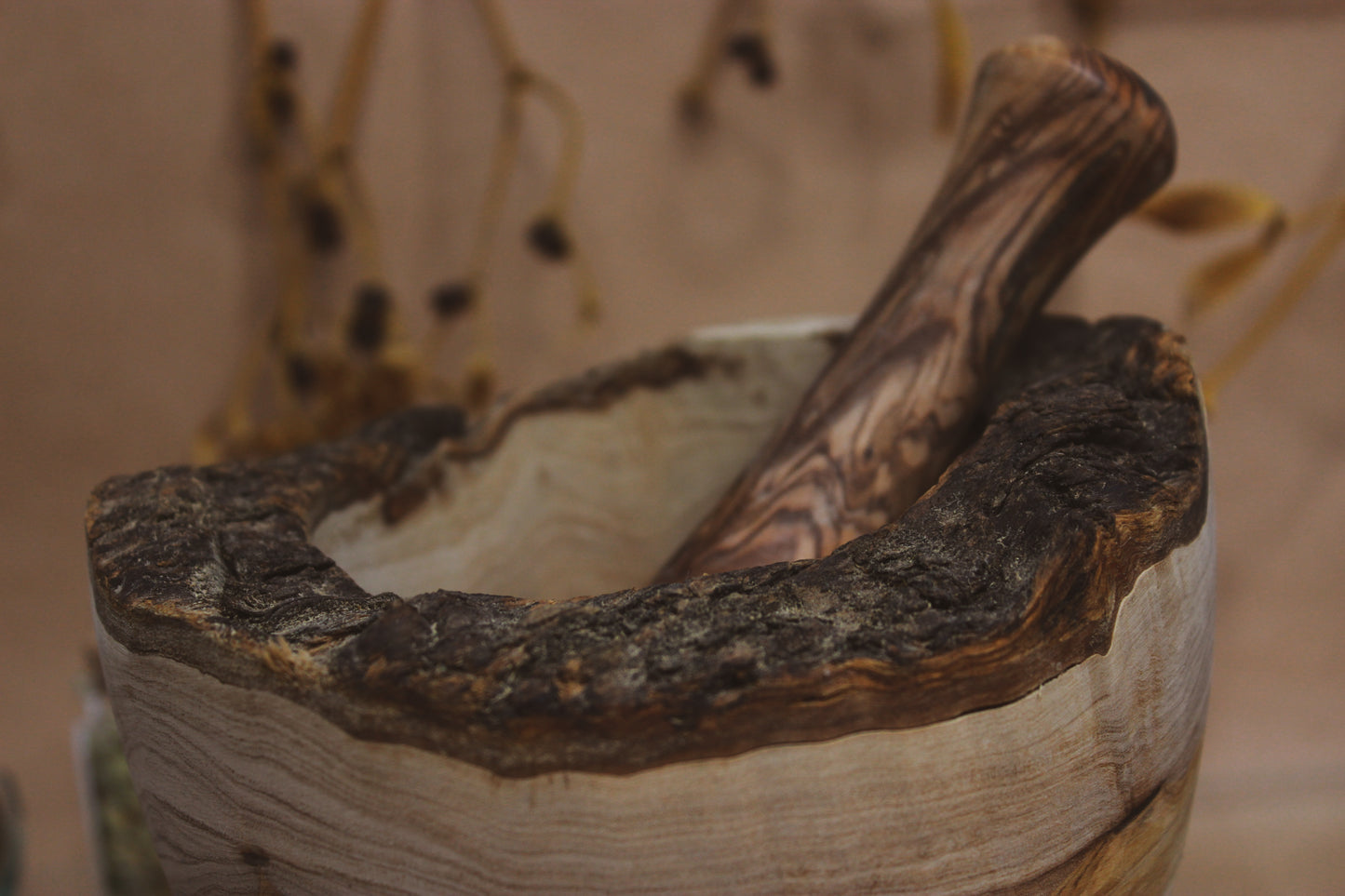 Nahaufnahme Mörser & Stößel aus Olivenholz - dunkler Rand mit Rinde, der Stößel ist ebenfalls dunkler als das restliche Holz in dem er sich befindet