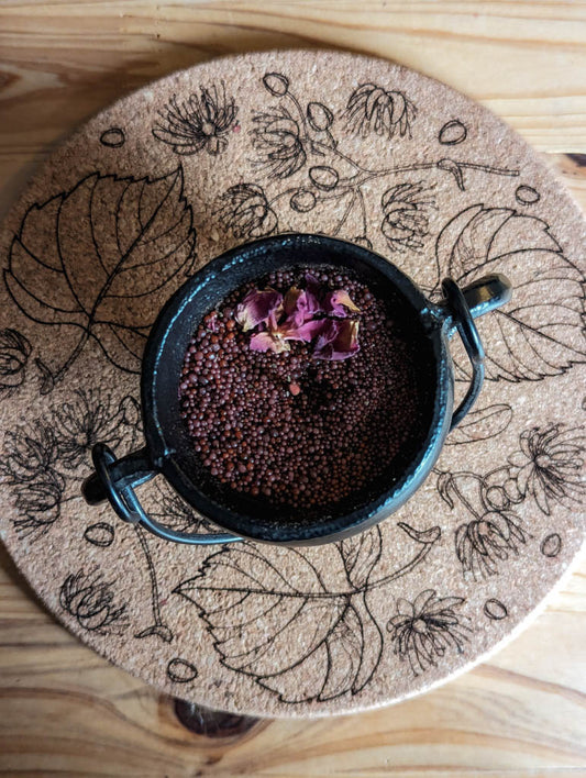 Auf einem Korkuntersetzer steht ein Kessel mit rotem Kerzensand und Rosenblüten darin.