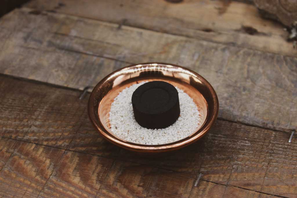 Eine Kupferschale mit Sand gefüllt und einem Stück Räucherkohle darin.