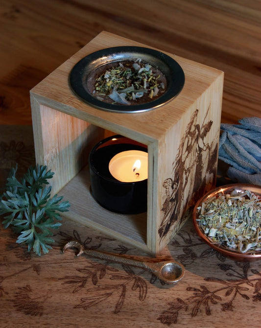 Das Räucherwerk Bannrauch auf einem Sieb eines Stövchens aus Holz. Daneben eine Kupferschale mit dem gleichen Räucherwerk, sowie zur Dekoration Wermut und Salbei. Vor dem Stövchen liegt ein schöner Rituallöffel oder Räucherlöffel mit einer Mondsichel am Griff.