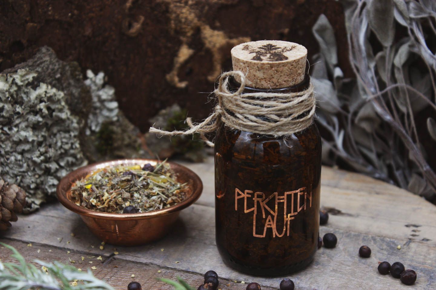 Räucherwerk in einem Braunglas mit Korken. Darauf steht in kupferner Schrift Perchtenlauf. Daneben steht eine Kupferschale gefüllt mit Räucherwerk. Drumherum liegen Wacholderbeeren verstreut.