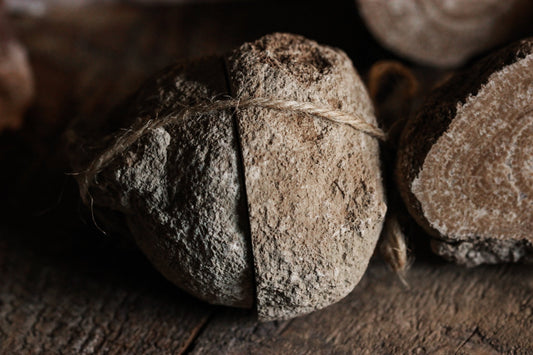 Eichenberger Kugel, Aragonit-Paar aus Österreich -Eichenberger Kugel, Aragonit-Paar aus Österreich - Das Bild zeigt einen runden Aragoniten und einen geschnittenen Aragoniten auf einer gealterten Holzoberfläche. Der Aragonit hat eine raue Textur und ist braun. Die anderen Aragoniten zeigt deutliche Ringe und haben eine texturierte Oberfläche. Die Schnur, die den Aragonit bindet, ist dünn und wirkt rustikal. Die gealterte Holzoberfläche unter diesen Objekten hat sichtbare Körner und Texturen.