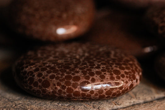 Kalkoolith Scheibenstein aus Deutschland - Kalkoolith Scheibenstein, Das Bild zeigt eine Nahaufnahme von mehreren Kalkolithen mit einer einzigartigen porösen Textur. Die Kalkolithen sind dunkelbraun und haben eine stückige Oberfläche, die sehr detailliert und sichtbar ist. Sie liegen auf einer Holzoberfläche, die sichtbare Körner und Texturen aufweist.