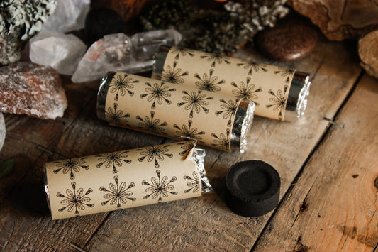 Kohle zum Räuchern - Räucherzubehör - Rollen mit Räucherkohle umwickelt in einem Papier welches das Hollenkraut Logo trägt, schwarze ausgepackter Räucherkohle auf einem hölzernen Hintergrund