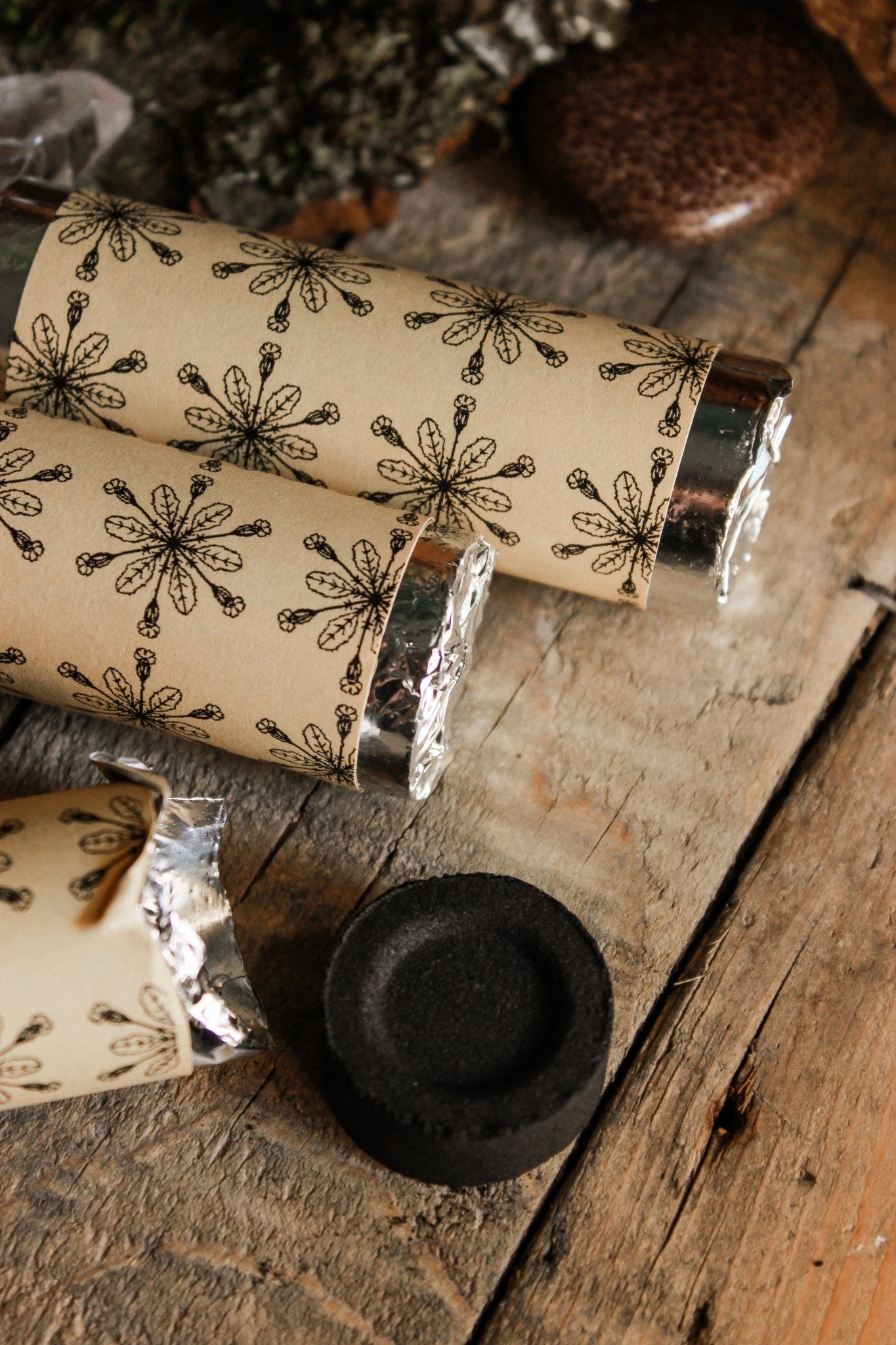 Kohle zum Räuchern - Räucherzubehör - Rollen mit Räucherkohle umwickelt in einem Papier welches das Hollenkraut Logo trägt, schwarze ausgepackter Räucherkohle auf einem hölzernen Hintergrund