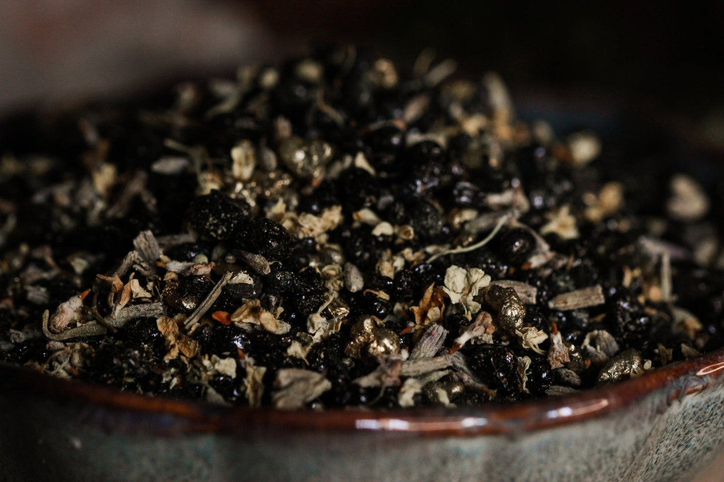 Nahaufnahme Räucherwerk Pech & Gold. Es sind einzelne Kräuter wie Holunder und Lavendel zu erkennen. Außerdem schwarze und goldene Harz-Stücke.