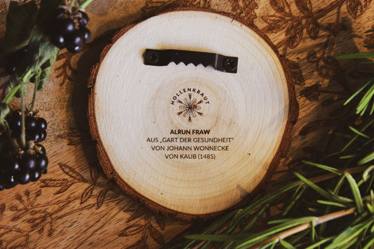 Handgefertigtes rundes Holzprodukt mit graviertem Text ‘HOLLENKRAUT ALRUN FRAW AUS „GART DER GESUNDHEIT“ VON JOHANN WONNECKE VON KAUB (1485)’ und einem eleganten Design, umgeben von Brombeeren und grünen Blättern.