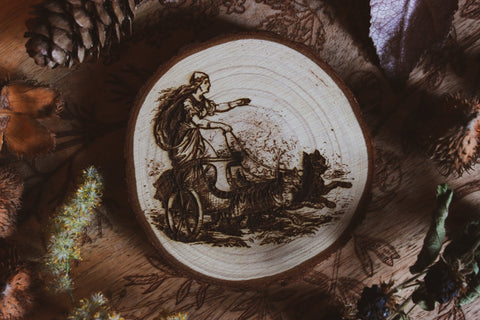 Wandbild aus Holz "Freyja im Katzenwagen" - Wandbild aus Holz "Freyja im Katzenwagen" - “Handgefertigtes Kunstwerk auf einem kreisförmigen Holzstück, das eine Freya auf einem Zugwagen darstellt, Katzen ziehen ihn Das Kunstwerk ist umgeben von Naturmaterialien wie Tannenzapfen und Blättern.