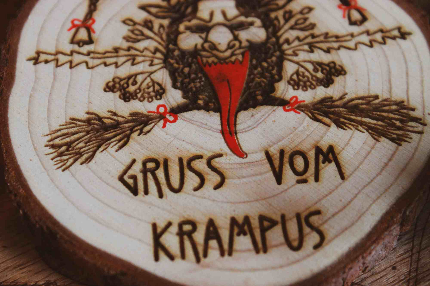 Wandbild aus Holz "Gruss vom Krampus" - Nahaufnahme Wandbild aus Holz "Gruss vom Krampus" - Handgefertigtes Krampus-Kunstwerk auf einem runden Holzstück. Krampus ist mit Hörnern und einer langen Zunge dargestellt, was die typische Darstellung der Folklore-Kreatur widerspiegelt. Der Schriftzug ‘GRUSS VOM KRAMPUS’ ist am unteren Rand eingraviert.