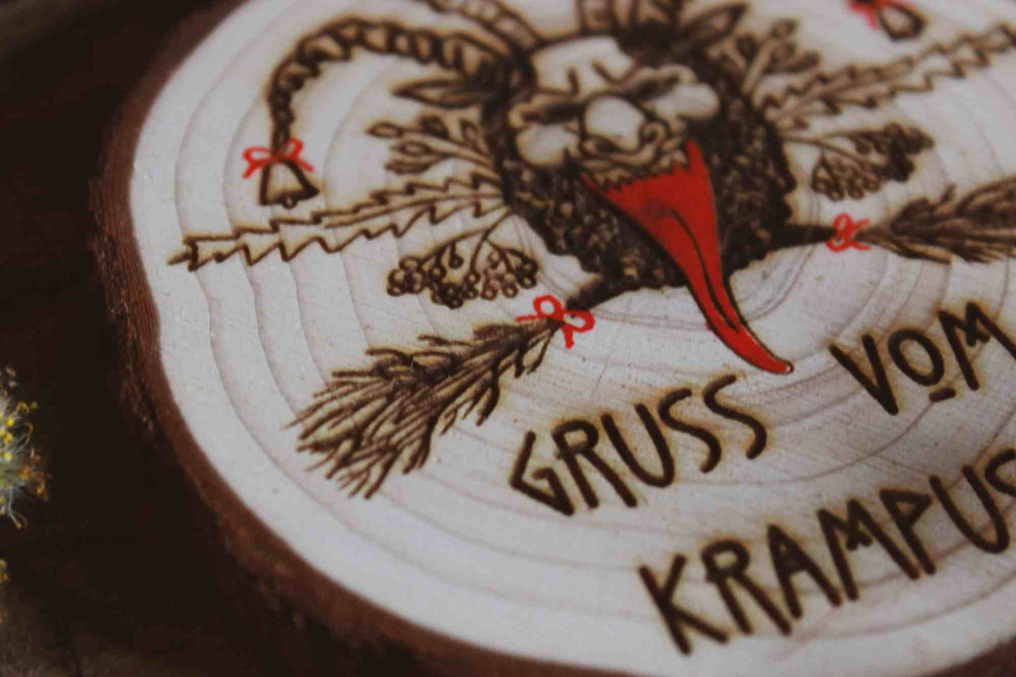 Nahaufnahme Wandbild aus Holz "Gruss vom Krampus" - Handgefertigtes Krampus-Kunstwerk auf einem runden Holzstück. Krampus ist mit Hörnern und einer langen Zunge dargestellt, was die typische Darstellung der Folklore-Kreatur widerspiegelt. Der Schriftzug ‘GRUSS VOM KRAMPUS’ ist am unteren Rand eingraviert.