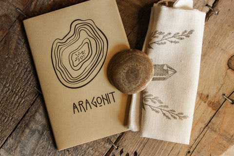 Aragonit Scheibenstein aus Österreich - Faire regionale Steine -ARAGONIT mit kleiner bedruckter Tasche und einem kleinen ARAGONIT Booklet auf einem Holztisch
