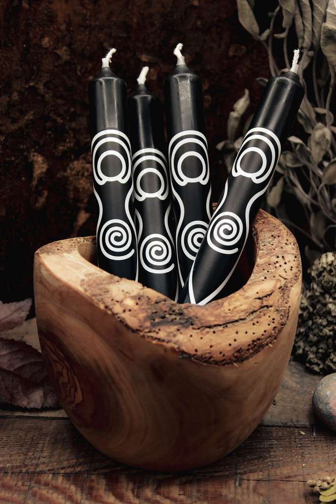 Vier schwarze Stabkerzen mit weißem Göttin-Motiv liegen in einer Holzschale.