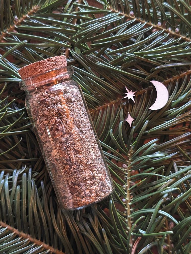 Eine Korkenflasche liegt gebettet auf Tannenzweigen. In der Flasche ist Beifuß zu sehen.