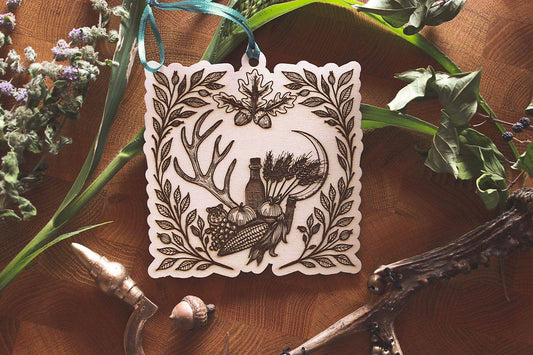 Herbstliches Holzornament zum Aufhängen mit filigraner Gravur zu Mabon. Zeigt Erntemotive wie Getreide, Mais, Eicheln und Trauben, sowie einen kleinen Hamster, eingerahmt von Hirschgeweihen, Hagebuttenzweigen und einer Erntesichel. Mit türkisfarbenem Band und rustikalem Flair. Ideal für saisonale Dekoration und spirituelle Rituale zur Herbsttagundnachtgleiche.