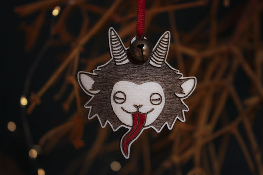 Vor einem Mistelstrauch hängt an einem roten Faden mit Glöckchen ein Holz-Ornament, das den niedlichen Kopf eines Krampus mit langer roter Zunge und Hörnern eingebrannt hat.