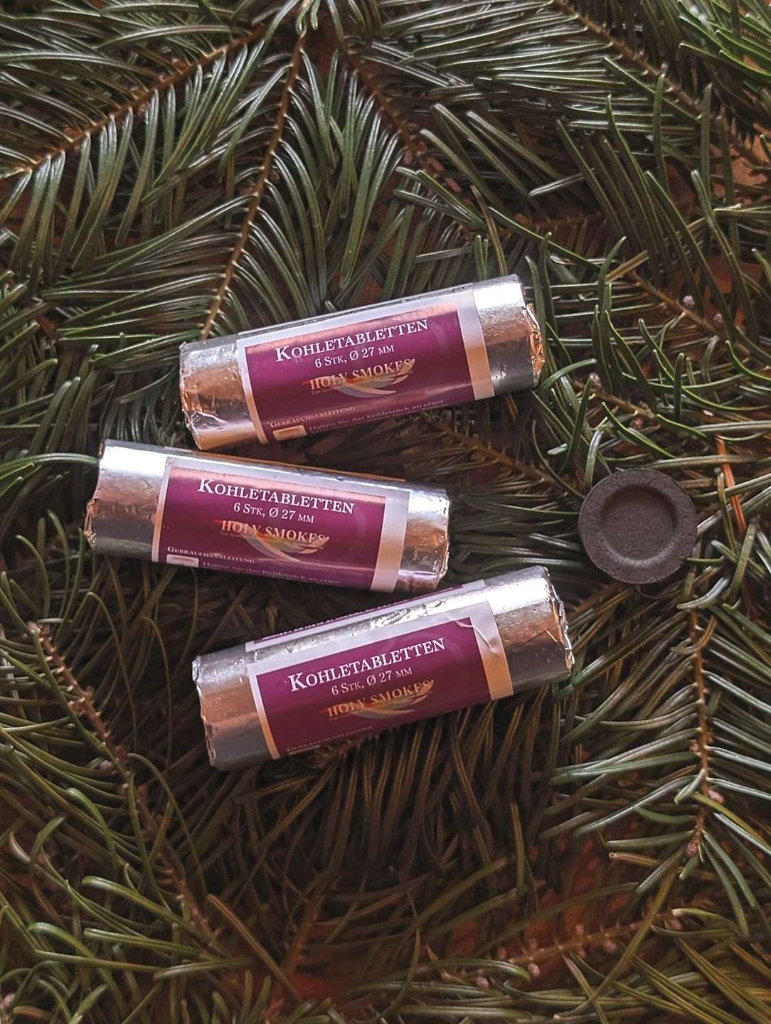 Drei Rollen Räucherkohle liegen auf Tannenzweigen.
