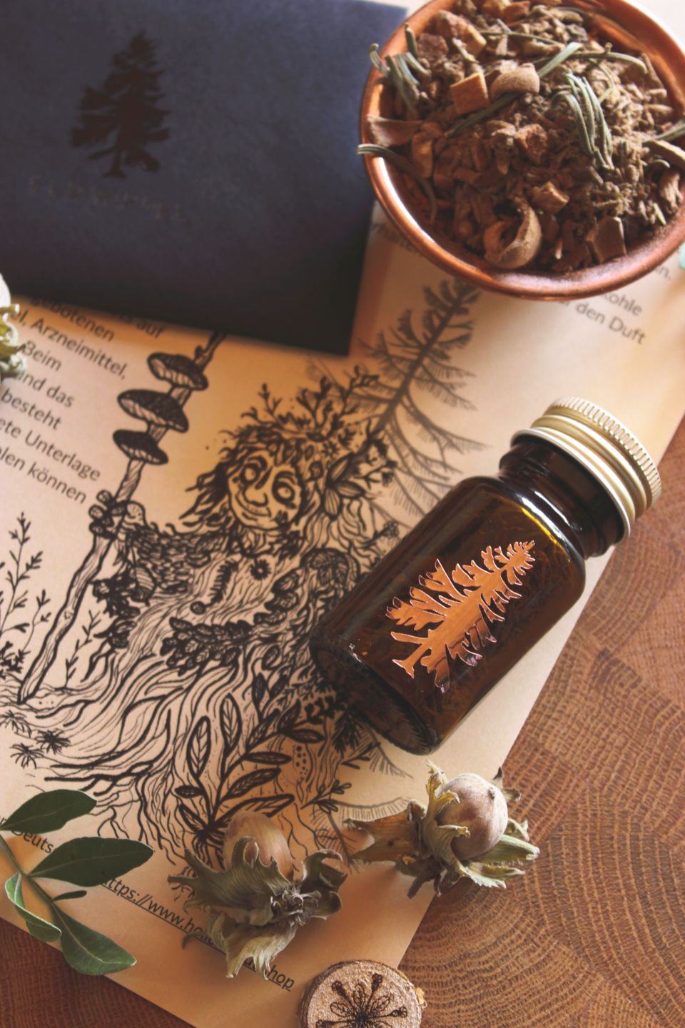 Rustikale Anordnung aus einer Braunglasflasche mit Baumemblem und Räucherwerk, einer Schale getrockneter Kräuter, einer detaillierten schwarz‑weißen Waldwesen‑Illustration (ein Moosweiblein) sowie Nüssen und Blättern auf Papier mit Schrift.