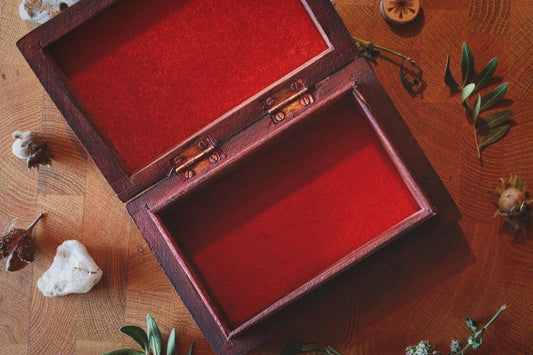 Geöffnete Holzkiste für Tarotkarten mit rotem Samtfutter, umgeben von Naturmaterialien wie Blättern, Steinen und Holzscheiben. Die Kiste liegt auf einer hölzernen Oberfläche und wirkt wie eine liebevoll arrangierte, rituelle Aufbewahrungsstätte.