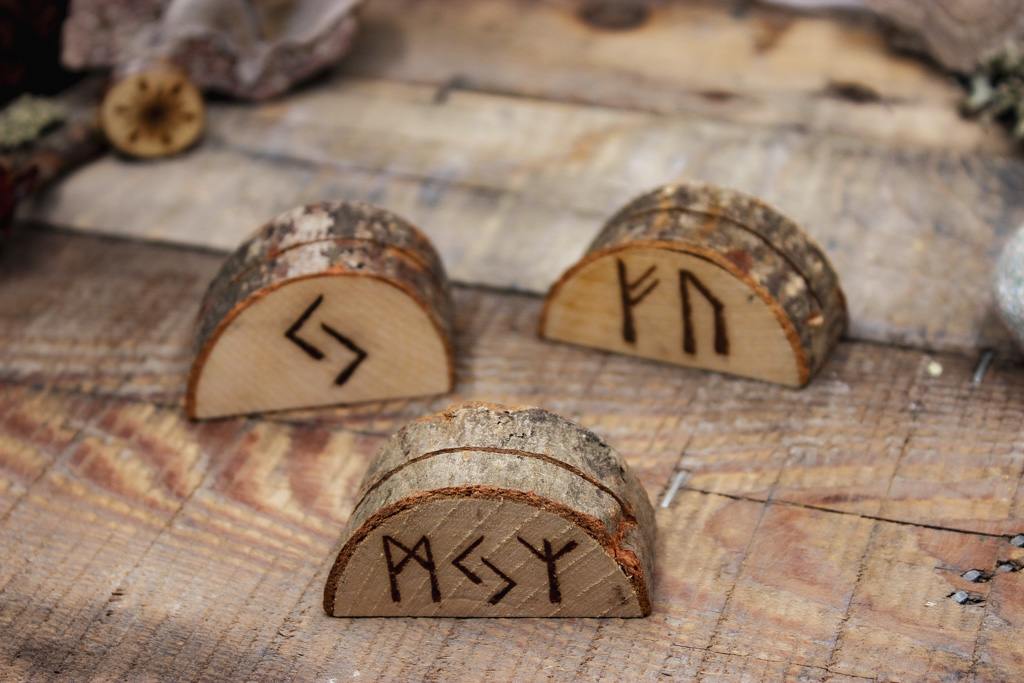 Drei Kartenhalter aus Holz stehen auf einem Holztischchen. Die Kartenhalter haben eine rustikale Rinde. Eingebrannt haben sie verschiedene Runen.