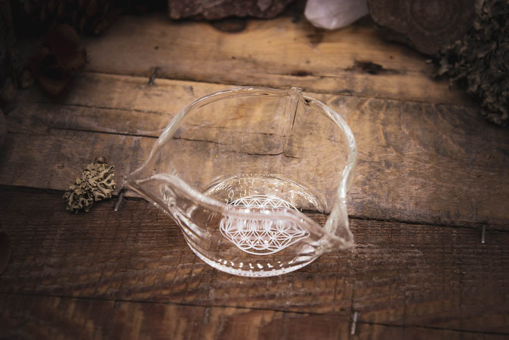 Kleiner kunstvoll hergestellter gläserner Teil der Duftlampe, aufgestellt auf einem dunklen Tisch umgeben von Kräutern und KRistallen