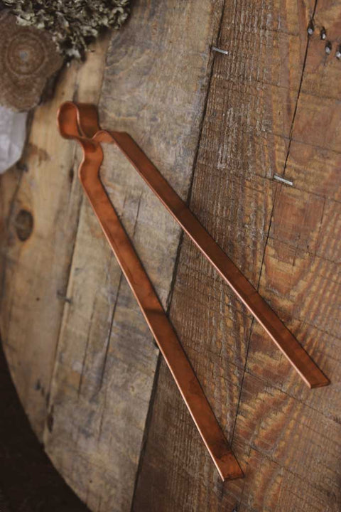 Eine Räucherzange aus Kupfer liegt auf einem Holzbrett.
